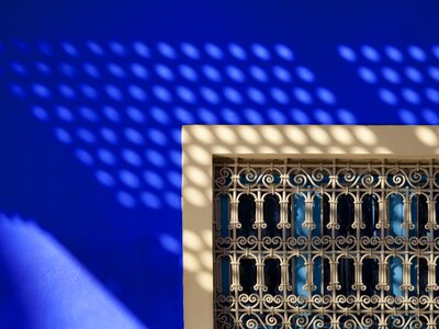 Detail of an Arabic window against a deep blue wall and shadows in Majorelle Gardens, Marrakech, Morocco