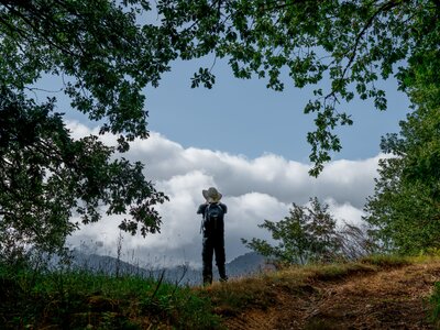 Hiker taking picture in distance with green tree branches framed around them, Picos De Europa, Spain