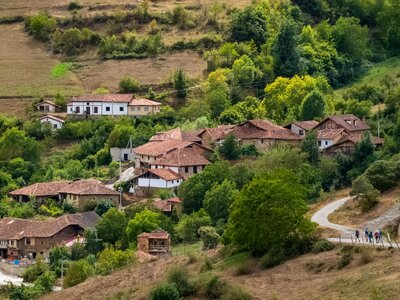 Distant view of village nestled in green mountainside with group of walkers moving towards it, Cantabria, Spain