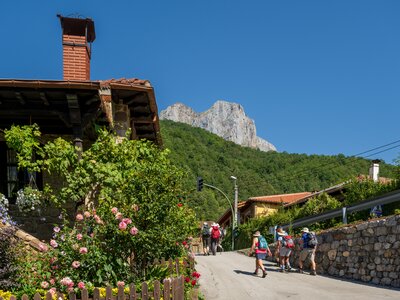 Walking holiday group walking up road in town with mountain in distance on sunny day with clear blue sky, Cantabria, Spain