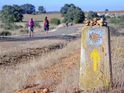 Yellow shell signpost and two people in background walking towards direction of Compostela Cathedral, Galicia, Spain, Camino de Santiago