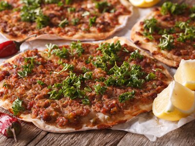 Close up of Turkish food lahmacun on a wooden table with chilli peppers and sliced lemon wedges next to meal