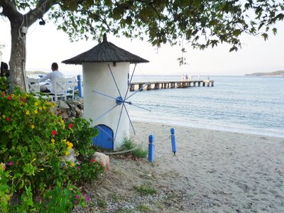 Mini Greek windmill on sandy beach with pier in background, Olympiada, Greece