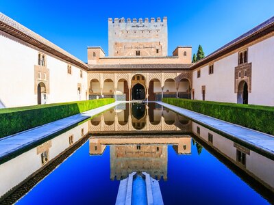 Symmetrical centre view of Alhambra Palace fortress reflected in long body of still water mostly covered in shadow with sun shining on Alhambra Palace, Granada, Spain