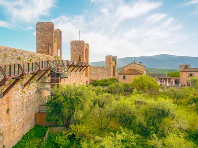 Interior of Monteriggioni medieval town on the hill with large wall fortification towering next to green grass with healthy trees, Tuscany, Italy