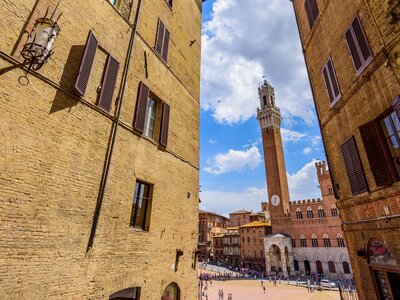 Old historic city Piazza del Campo in Siena with clocktower seen between gap of two buildings, Italy