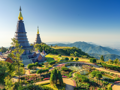 Two pagoda at the Inthanon mountain with winding pathways surrounded by colourful flowers, plants, and trees with mountainous landscape and hazy blue sky in distance, Chiang Mai, Thailand