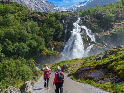 People on Ramble Worldwide cruise and walk holiday The Fjords of Norway walking towards Briksdalsbreen waterfall in distance with Briksdal glacier in far background, Norway, Europe