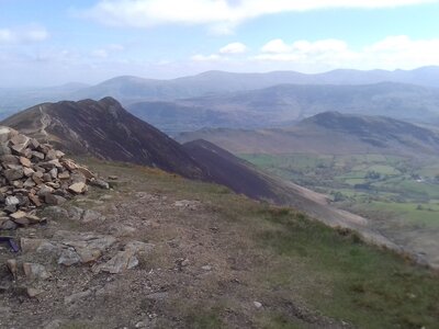 Hiking bag placed next to pile of rocks on Causey Pike Fell wit expansive yet cloudy view of Lake District mountainous landscape, England, UK