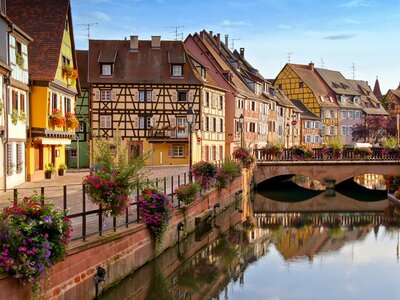 Late day view with half timbered houses, flowers, bridge and reflections in canals, Colmar, France