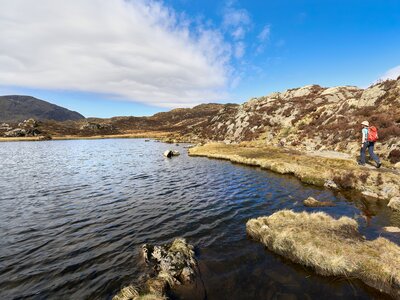 Female hiker walking alongside Innominate Tarn near summit of Hay Stacks, Lake District