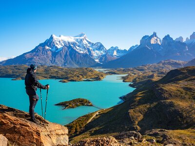 Hiker near cliff edge staring at snow-capped mountains using walking poles to stand firm, Torres del Paine national park, Patagonia, Chile