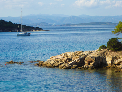 Boat in distance with faint view of mountains in far background on sunny day, Sardinia, Italy