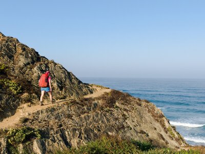 Woman with red backpack walking on the coastal trail, fishermen's trail in portugal