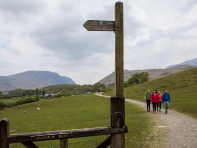 Walking group on walking trail moving towards signpost, Lake District, Cumbria, England