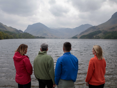 Four hikers standing by Buttermere Lake shore admiring view of peaks, Lake District