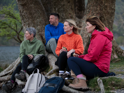 Group of four walkers sat under tree near Buttermere Lake enjoying lunch break