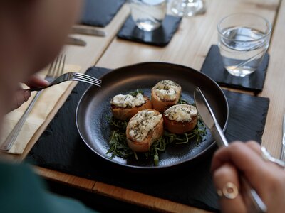 Over-shoulder view of plate of bruschetta with tasty toppings on wooden dining table at Hassness House