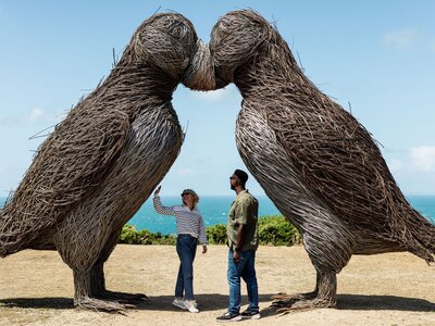 Couple standing beneath shadow of Plemont Bay Puffin Statues on sunny day, Jersey