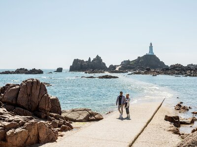 Couple following diminishing footpath with Corbiere Lighthouse in distance, Jersey, Channel Islands, United Kingdom