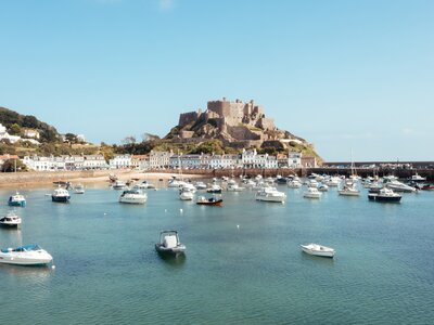 Turquoise-coloured harbour filled with scattering of small boats and Mont Orgueil Castle in distance, Jersey