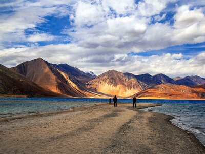 Silhouettes of people in distance standing by Pangong Tso Lake of Ladakh