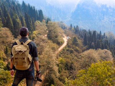 Male hiker with a camera in hand enjoys an aerial view of scenic Himalaya mountain landscape near Kolakham hill station, in the district of Kalimpong, India