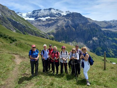 Ramble Worldwide walking group on walking holiday A Swiss Summer posing on grassy mountain walking trail and smiling with mountains in background on sunny day, Switzerland