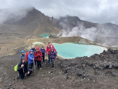 Group of ramble worldwide walkers smiling for camera together at Tongariro Crossing near vibrant emerald lakes at active volcano site, Tongariro National Park, a UNESCO Dual World Heritage Site, New Zealand