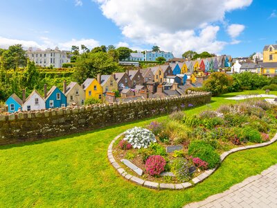 Row of brightly painted town homes on sunny day, seen from the Garden of Reflection park in the coastal town of Cobh, Ireland