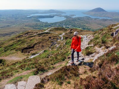 A hiker climbing Diamond Hill in Connemara National Park, admiring the sweeping views of lakes, mountains, and lush Irish wilderness