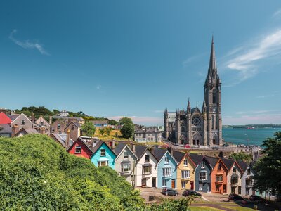 Colourful row of town houses with church in distance on sunny day in Cobh, Ireland