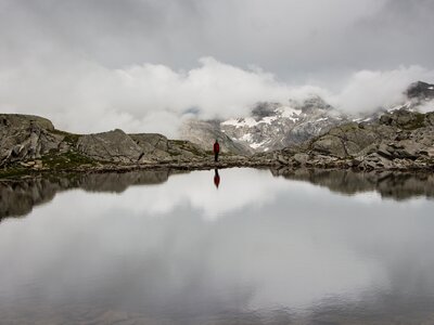 Hiking in Saas valley around Mattmark lake during cloudy day with clouds being reflected in still lake, Switzerland