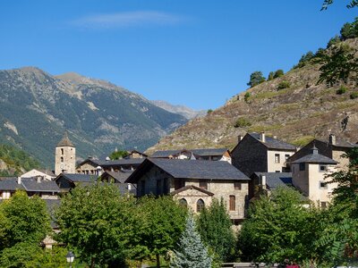 Stone houses and church in Ordino with mountain in background and lush green trees in foreground, Andorra