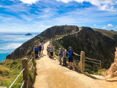 Ramble Worldwide walking group leaning against winding isthmus la coupee, Channel Islands, Sark