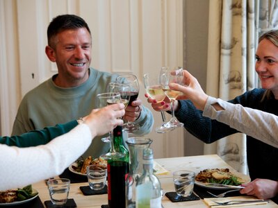 Happy people holding wine glasses to clink across dining table as a toast during meal at Hassness House in the Lake District
