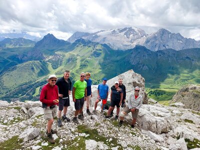 Ramble Worldwide leader Nick Conway leading walking group in the Dolomites, Italy, with all stood atop mountain with mountainous landscape surrounding