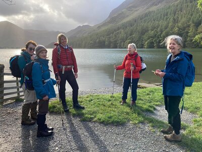 Group of women on walk in lake district near lake with sun shining through clouds, ramble worldwide walking holiday womens activity week