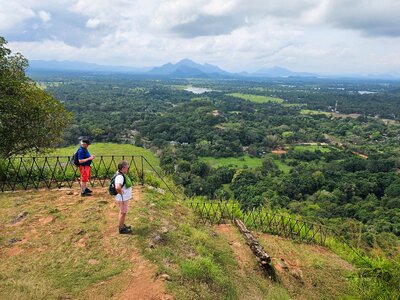 Two hikers on ramble worldwide walking holiday in Sri Lanka admiring green landscape with mountains in far distance on cloudy day