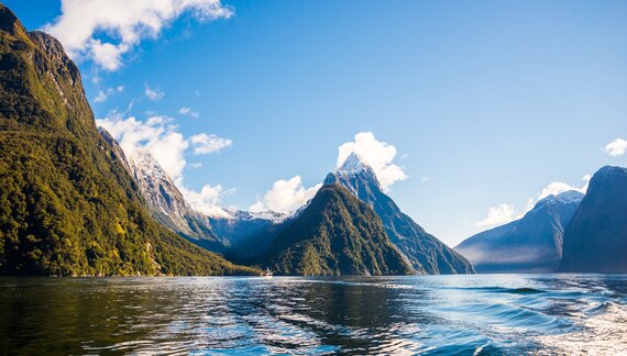 Low angle of water reflecting bright blue sky with clouds with mountainous landscape surrounding, Milford Sound Piopiotahi Fiord, Fiordland, New Zealand