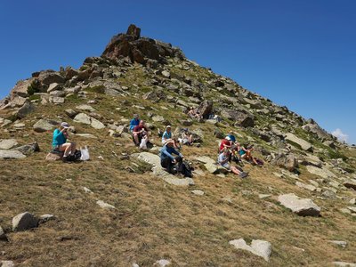 Ramble Worldwide hiking group resting on rocks on Pic Alt del Griu amidst clear blue skies with sunny weather, Andorra, Europe