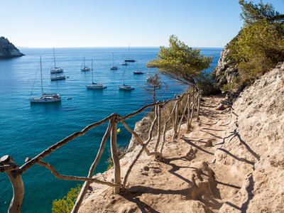 Coastal walk from beach in Menorca with small boats floating in sea in distance, Spain