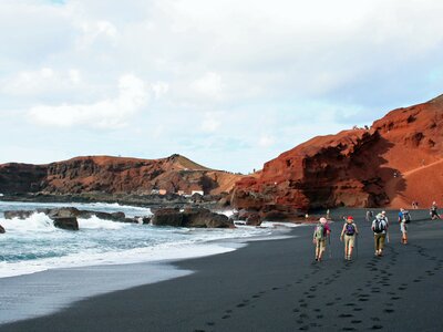 Small walking group walking along black sand beach at El Golfo, Lanzarote, Spain, Europe