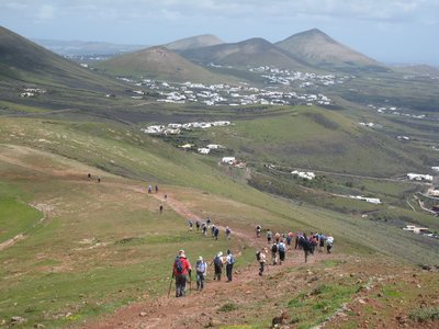 Walking group descending trail with white buildings and green peaks in distance, Lanzarote, Spain