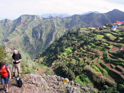 View of green mountainous terrain with people walking out of shot and village atop mountain in distance, Tenerife, Spain