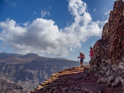 Two hikers descending La Merica following bending footpath casted in shadow from tall rock next to them with mountainous terrain in background, La Gomera, Canary Island, Spain (Chris Jagan).jpg