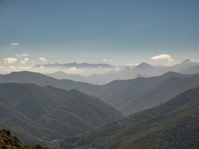 Mountainous landscape of Picos De Europa mountain range with clouds hovering close by to layered mountain outlines and blue skies above, Spain
