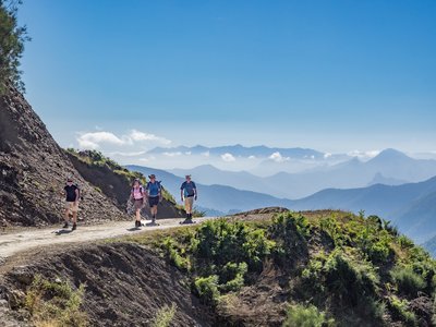 Group of four people on Ramble Worldwide walking holiday descending hill in Picos De Europa mountain range in Spain with clear blue sky on sunny day and layered gradient outlines of mountains in background