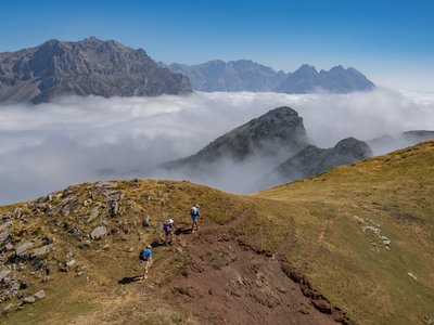 Aerial view of three hikers ascending slope on mountain ridge with sea of white clouds and mountain peaks poking through, Picos De Europa, Spain