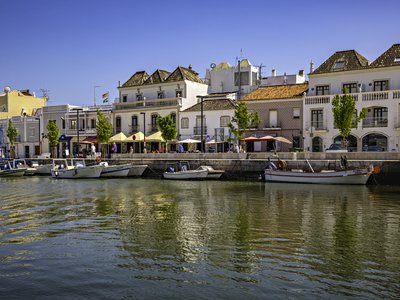 Boats docked alongside river near row of buildings, Tavira, Portugal